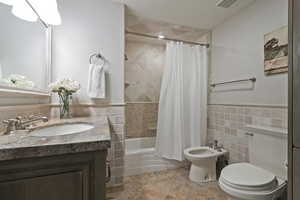 Bathroom featuring vanity, toilet, shower / bath combo with shower curtain, a bidet, and tile walls