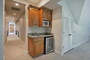 Indoor bar featuring wine cooler, light colored carpet, white microwave, baseboards, and recessed lighting