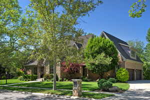 View of property hidden behind natural elements with brick siding, driveway, a garage, and a front lawn