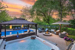 Pool at dusk with an outdoor living space with a fire pit, a gazebo, a patio, and a hot tub
