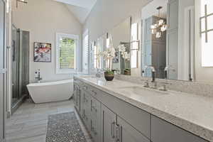 Bathroom with double vanity, a soaking tub, a chandelier, a stall shower, and vaulted ceiling