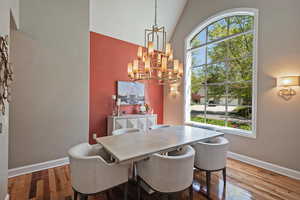 Dining space featuring a chandelier, wood finished floors, baseboards, and high vaulted ceiling