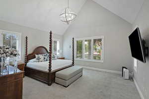 Bedroom with a chandelier, multiple windows, high vaulted ceiling, baseboards, and light colored carpet