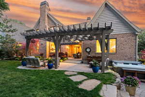 Back of house at dusk with brick siding, a pergola, a chimney, and a patio