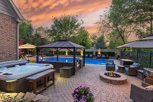 Patio terrace at dusk featuring a hot tub, a gazebo, an outdoor fire pit, and a patio area