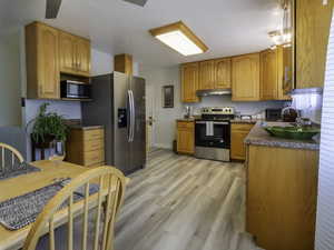 Kitchen with appliances with stainless steel finishes, under cabinet range hood, light wood finished floors, a sink, and baseboards