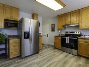 Kitchen with stainless steel appliances, under cabinet range hood, light wood-type flooring, and brown cabinetry