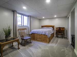 Bedroom with light colored carpet, a paneled ceiling, recessed lighting, baseboards, and a wood stove