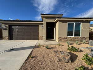 Prairie-style house featuring stone siding, stucco siding, driveway, and an attached garage