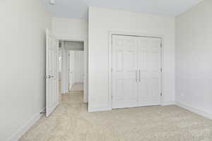 Unfurnished bedroom featuring light carpet and a closet