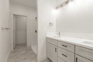Bathroom with tiled shower, double vanity, wood finished floors, and baseboards