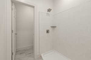 Full bath featuring a tile shower, baseboards, and wood finished floors