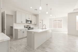 Kitchen with appliances with stainless steel finishes, a sink, a kitchen island with sink, baseboards, and recessed lighting