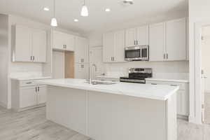 Kitchen with appliances with stainless steel finishes, a sink, recessed lighting, light stone counters, and decorative light fixtures