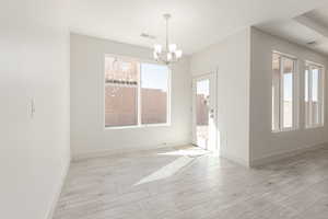Spare room with a chandelier, light wood finished floors, and baseboards