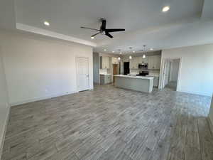 Unfurnished living room with recessed lighting, a raised ceiling, light wood finished floors, and a ceiling fan