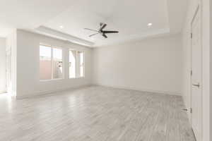 Empty room featuring a tray ceiling, ceiling fan, light wood-style flooring, recessed lighting, and baseboards
