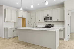 Kitchen featuring stainless steel appliances, light wood-type flooring, recessed lighting, hanging light fixtures, and a kitchen island with sink