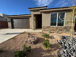 View of front of property with stone siding, concrete driveway, stucco siding, and an attached garage