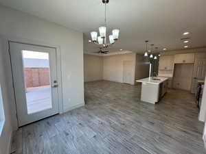 Kitchen with hanging light fixtures, an island with sink, a chandelier, open floor plan, and light wood-style floors