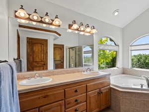 Full bath featuring double sink vanity, a shower stall, a bath, and vaulted ceiling