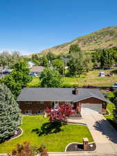 View of front of house with a mountain view, concrete driveway, brick siding, a front lawn, and an attached garage
