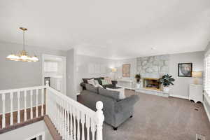 Carpeted living area with baseboards, a stone fireplace, and a chandelier
