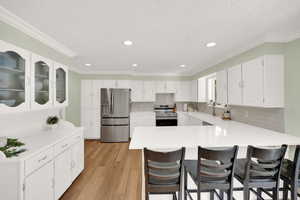 Kitchen with stainless steel appliances, a peninsula, a kitchen breakfast bar, light wood-style flooring, and decorative backsplash