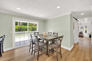 Dining space featuring a barn door, light wood-type flooring, ornamental molding, recessed lighting, and baseboards