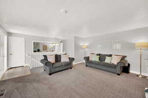 Carpeted living area with a chandelier, baseboards, and a textured ceiling