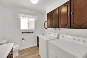Laundry area with independent washer and dryer, light wood-style floors, and baseboards