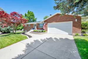 Ranch-style house with brick siding, concrete driveway, a garage, and a front lawn