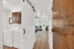 Hall with a barn door, separate washer and dryer, and light wood-style flooring