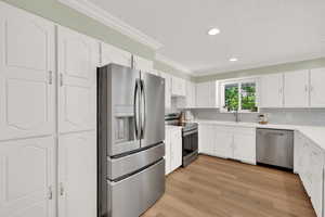 Kitchen featuring appliances with stainless steel finishes, a sink, ornamental molding, a textured ceiling, and white cabinetry