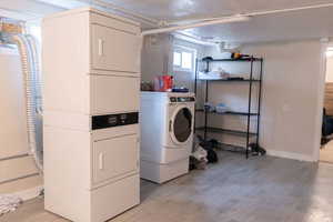 Laundry area featuring stacked washer and clothes dryer, light wood finished floors, and baseboards