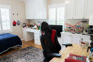 Bedroom featuring light wood-style floors, a desk, and multiple windows