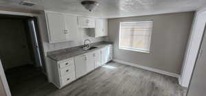 Kitchen featuring a sink, tasteful backsplash, baseboards, white cabinetry, and a textured ceiling