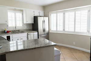 Kitchen featuring a sink, stainless steel appliances, decorative backsplash, baseboards, and light tile patterned flooring