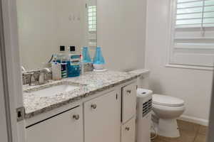 Half bathroom with vanity, toilet, plenty of natural light, and tile patterned flooring