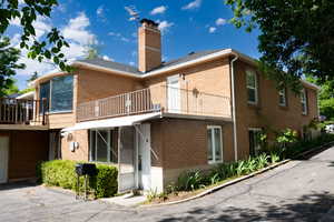 Rear view of property with a chimney, a balcony, brick siding, and a sunroom