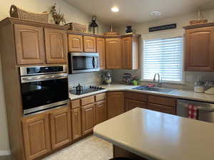 Kitchen with brown cabinetry, lofted ceiling, appliances with stainless steel finishes, light countertops, and a sink