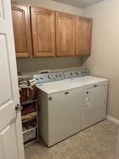 Laundry room featuring cabinet space, light tile patterned floors, baseboards, and independent washer and dryer