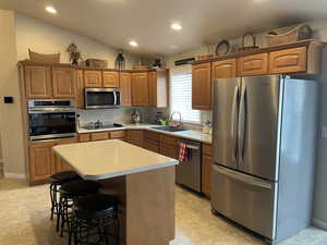 Kitchen featuring stainless steel appliances, a sink, a kitchen island, light countertops, and brown cabinets