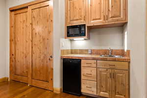 Kitchen with dark wood-style flooring, black microwave, light brown cabinetry, and tile counters