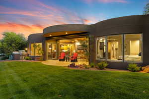 Back of house at dusk featuring stucco siding, an outdoor kitchen, a yard, and a patio area