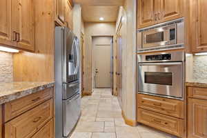 Kitchen with appliances with stainless steel finishes, baseboards, stone tile flooring, tasteful backsplash, and light stone countertops