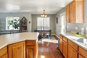 Kitchen with dark wood finished floors, light countertops, a chandelier, hanging light fixtures, and baseboards
