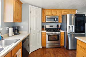 Kitchen featuring stainless steel appliances, light countertops, dark wood-style flooring, a textured ceiling, and a sink
