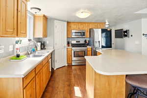 Kitchen with stainless steel appliances, a sink, light countertops, and dark wood-style floors