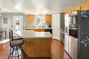 Kitchen featuring stainless steel appliances, light countertops, dark wood-style flooring, a sink, and a kitchen island